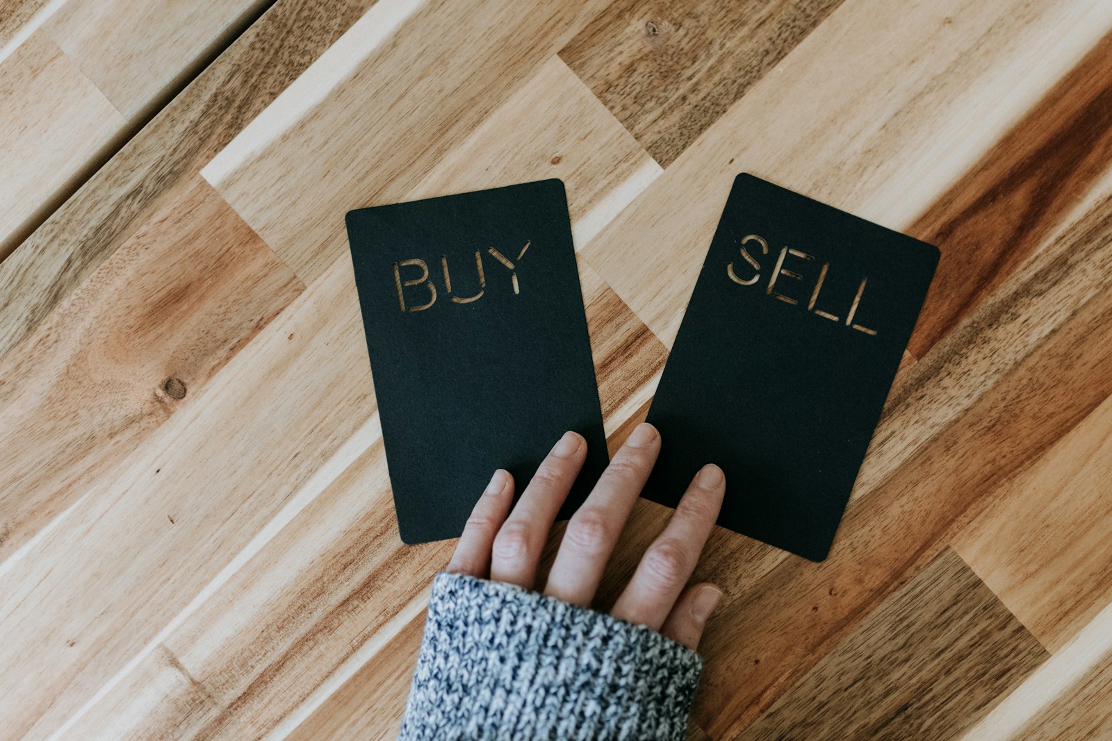 Photo by Kelly Sikkema a person holding two small black books with the words buy and sell on them